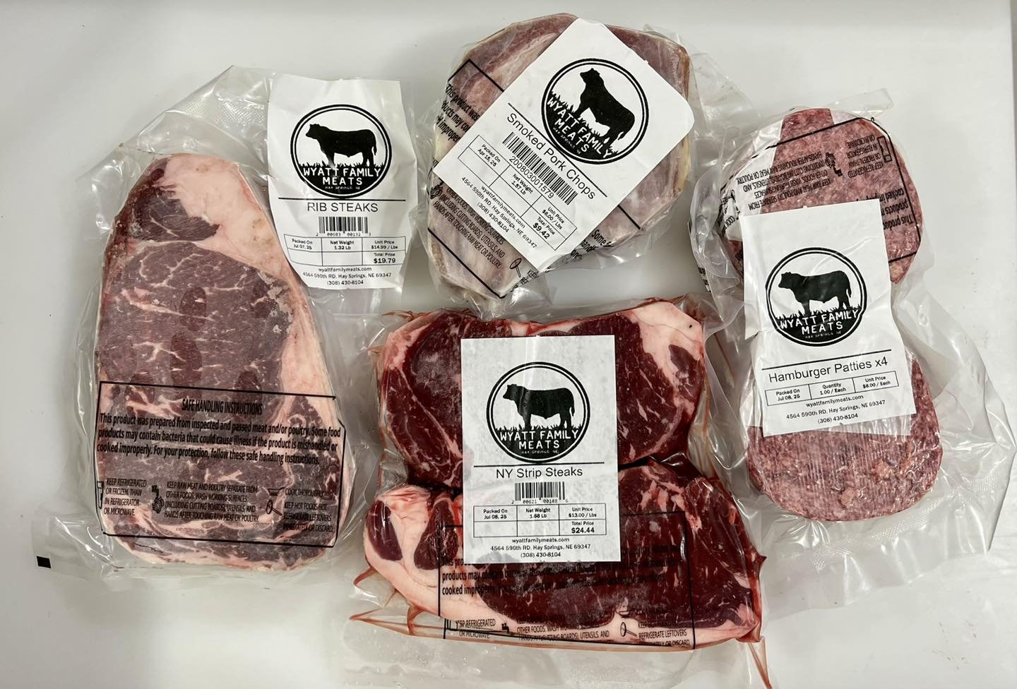 517127259_1193073659500663_7294805536528203576_n (1) Assorted packages of premium beef and pork products from Wyatt Family Meats, including rib steaks, NY strip steaks, smoked pork chops, and hamburger patties. Each package features clear labels with product details and handling instructions.