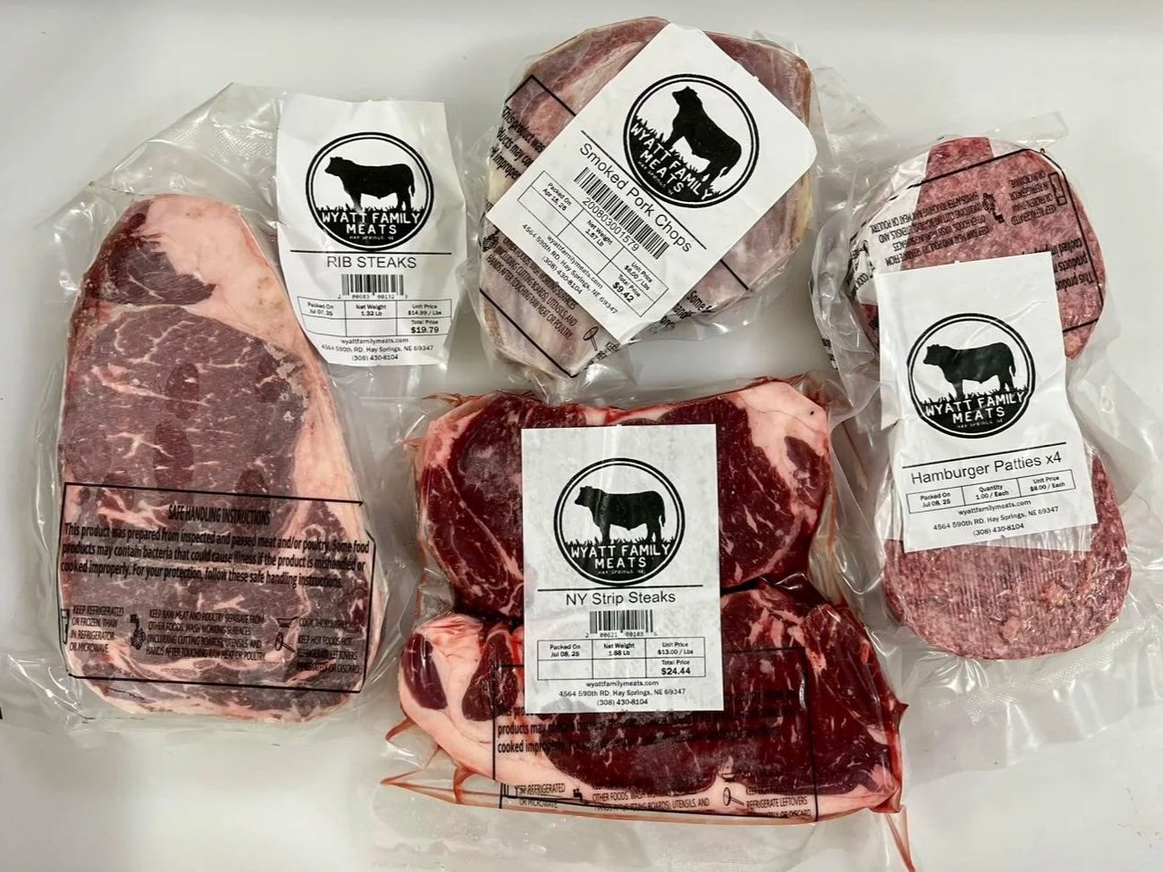 517127259_1193073659500663_7294805536528203576_n Assorted cuts of beef and pork from Wyatt Family Meats, including rib steaks, NY strip steaks, smoked pork chops, and hamburger patties, all packaged with labels detailing product information and handling instructions.