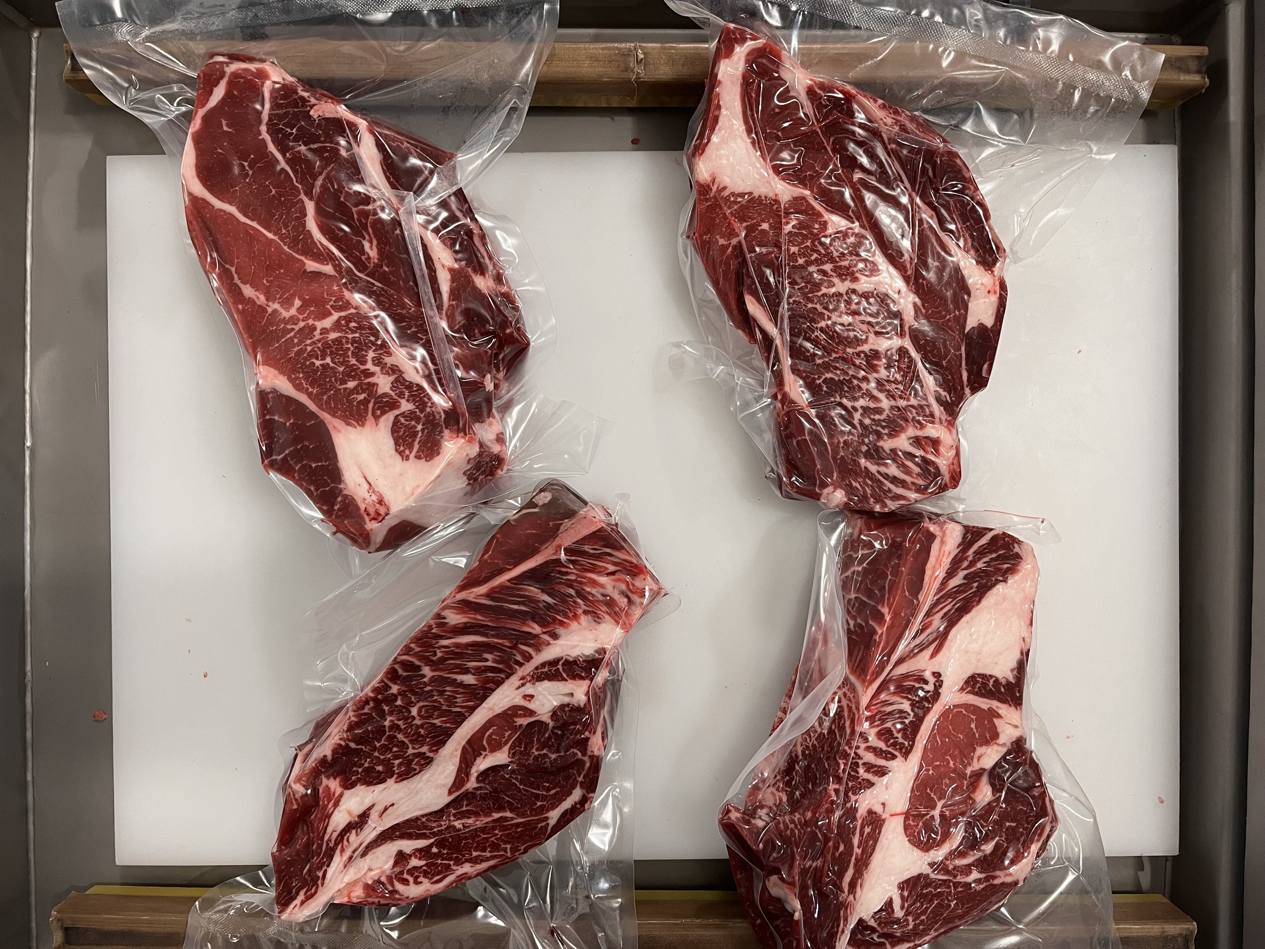 chuck+roasts Vacuum-sealed cuts of marbled beef on a white cutting board, showcasing high-quality meat ideal for grilling or slow cooking.