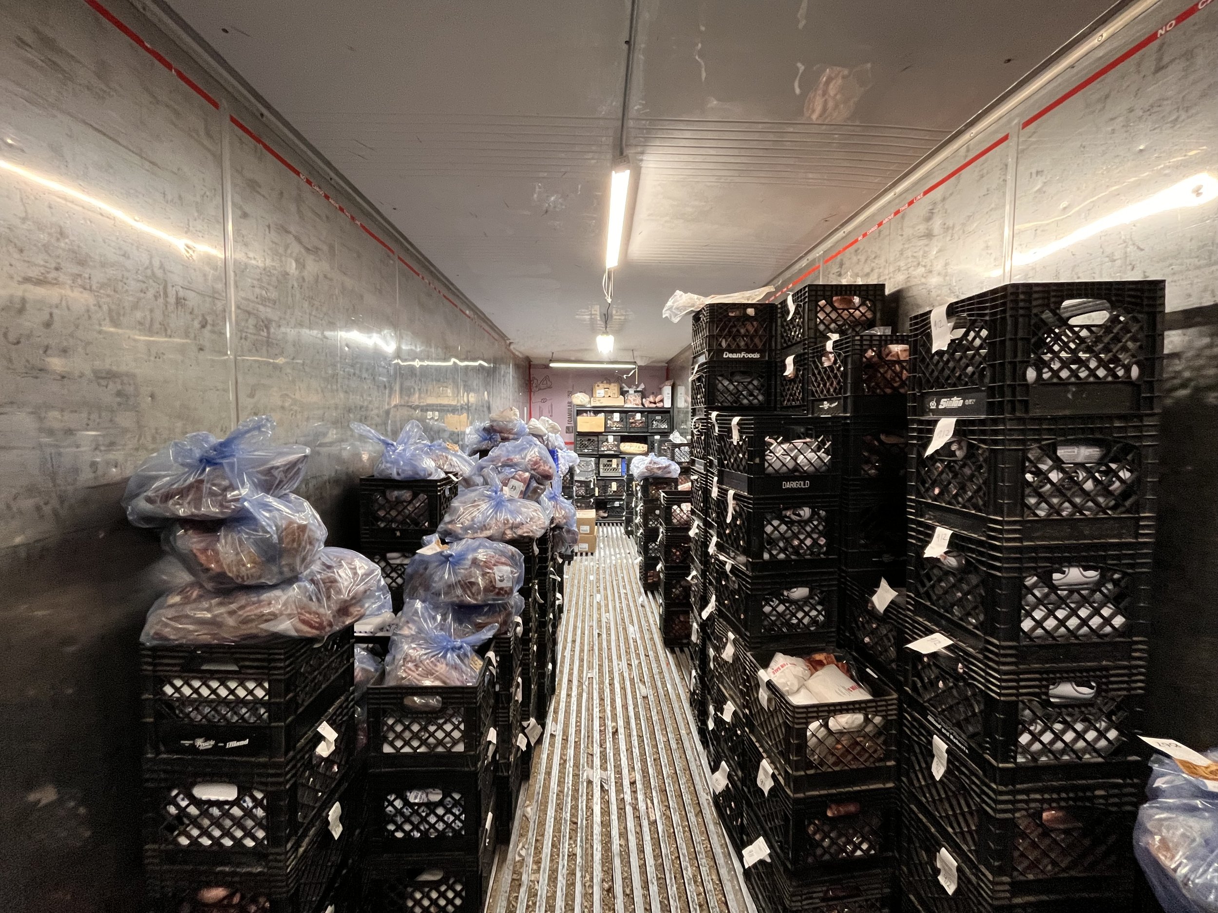 freezer Interior view of a refrigerated storage unit filled with stacked black crates containing food items, some covered with blue plastic bags, highlighting efficient food storage and organization in a commercial kitchen environment.