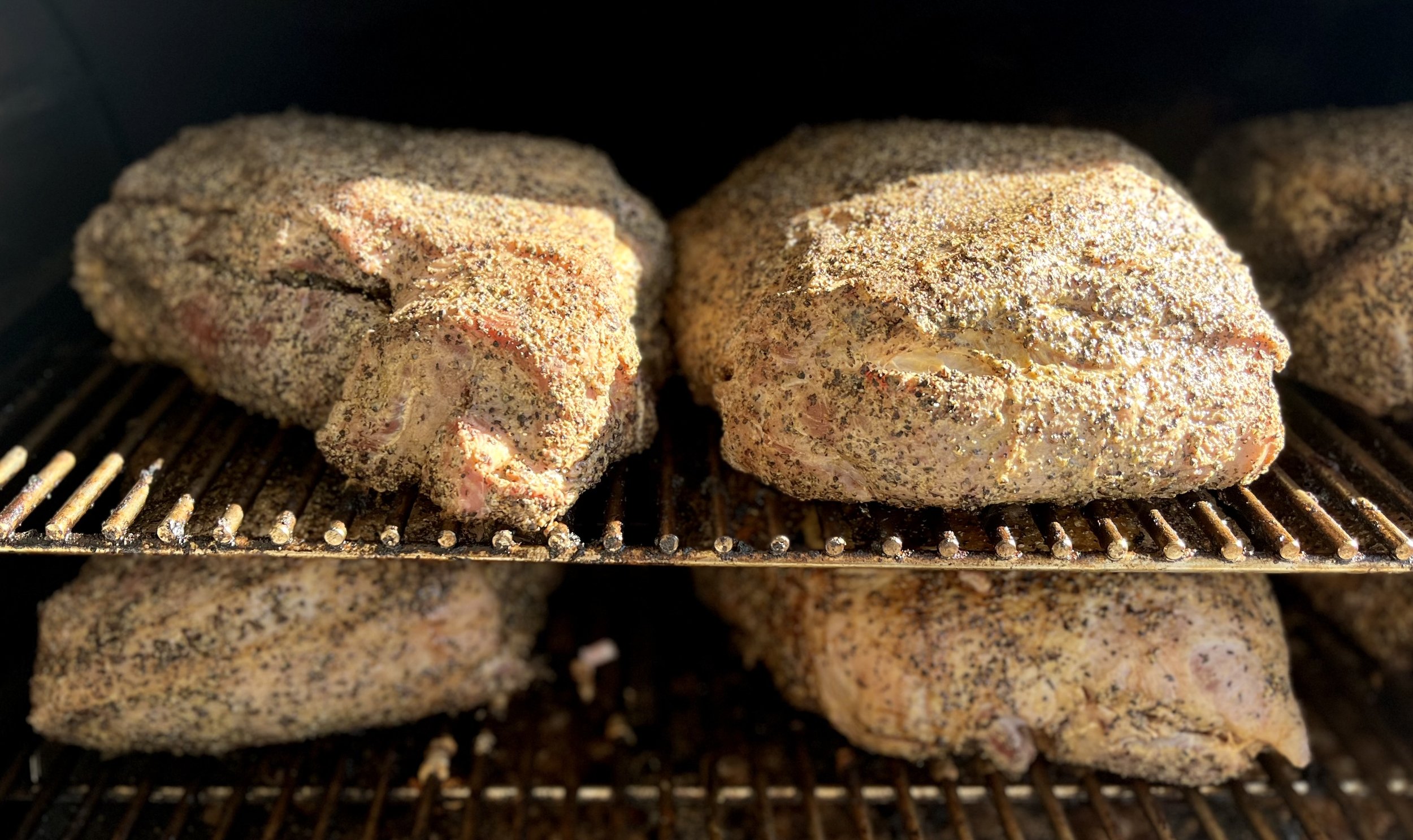 uncooked+pork+butts+on+smoker Smoked beef briskets seasoned with spices, resting on a grill rack in a smoker, showcasing a golden-brown crust and smoky flavor. Perfect for barbecue enthusiasts and meat lovers.